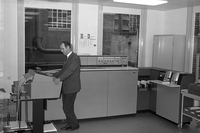 811058 Afbeelding van de heer J.W. Meijlis in de computerruimte van het Gebouw van het Gemeentelijk Energie- en ...